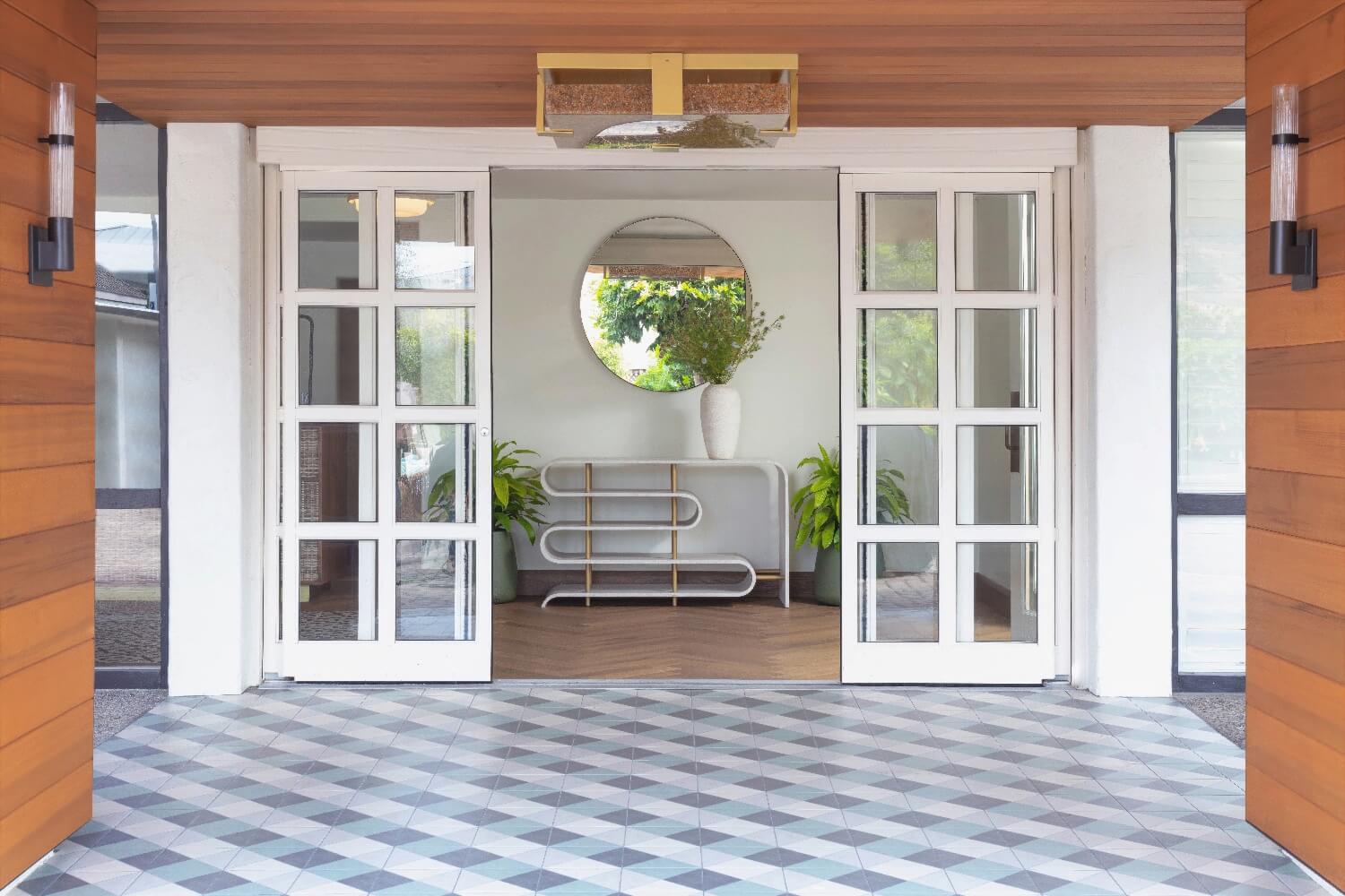 Hotel entrance at Carmel Mission Inn, Carmel, California, with geometric tile flooring, white French doors, and a round mirror over a console.