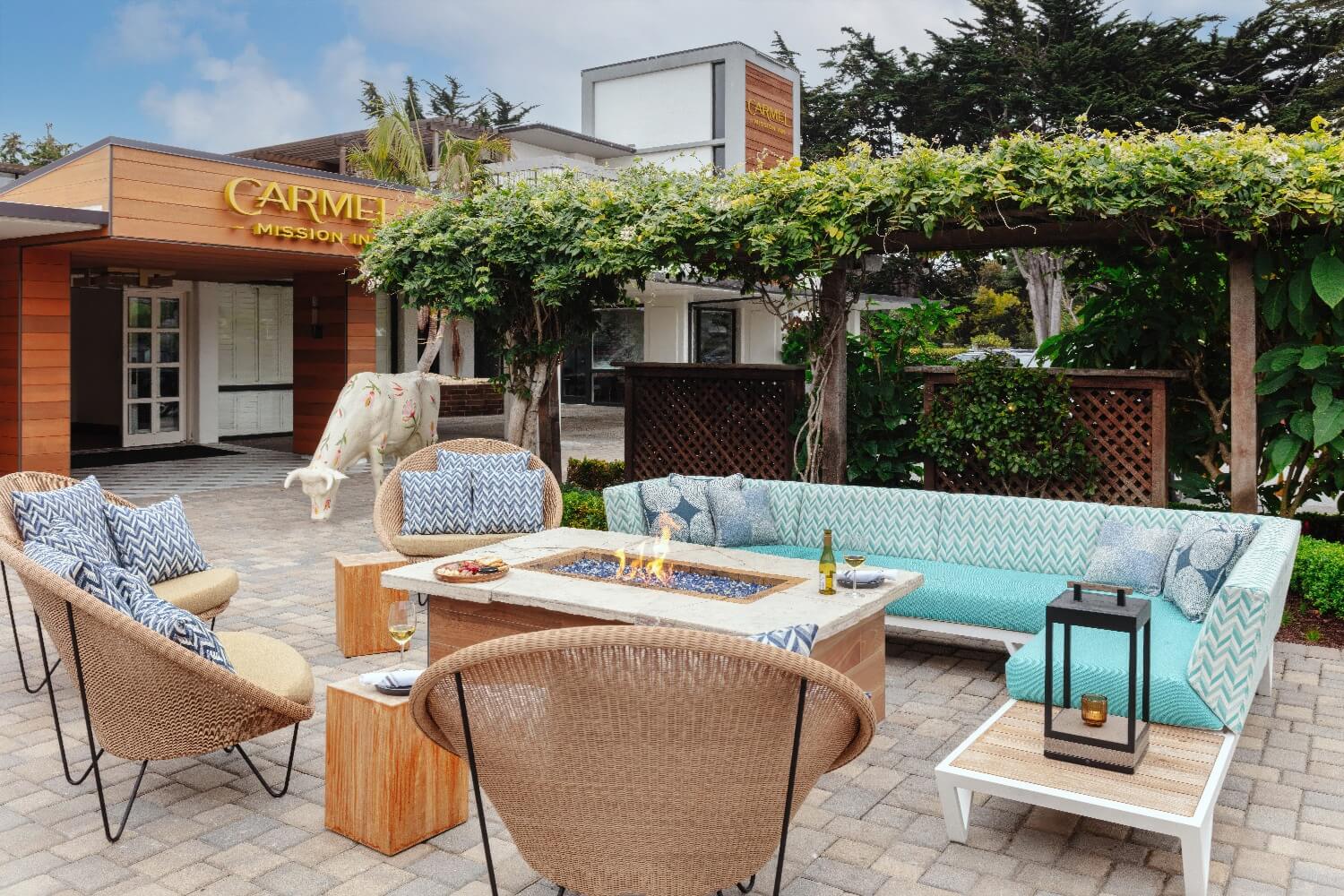 Fire-pit table with sectional and wicker seating in the entrance courtyard at Carmel Mission Inn, Carmel, California, with the painted cow sculpture by the lobby doors.