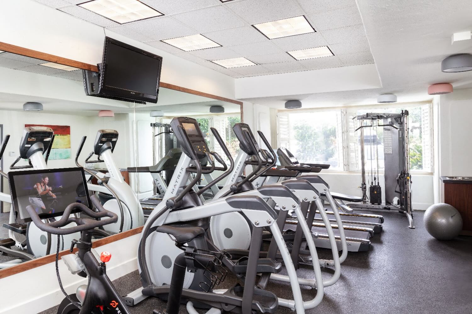 Fitness room at Carmel Mission Inn, Carmel, California, with a Peloton bike, elliptical machines, treadmills, and a cable weight station.