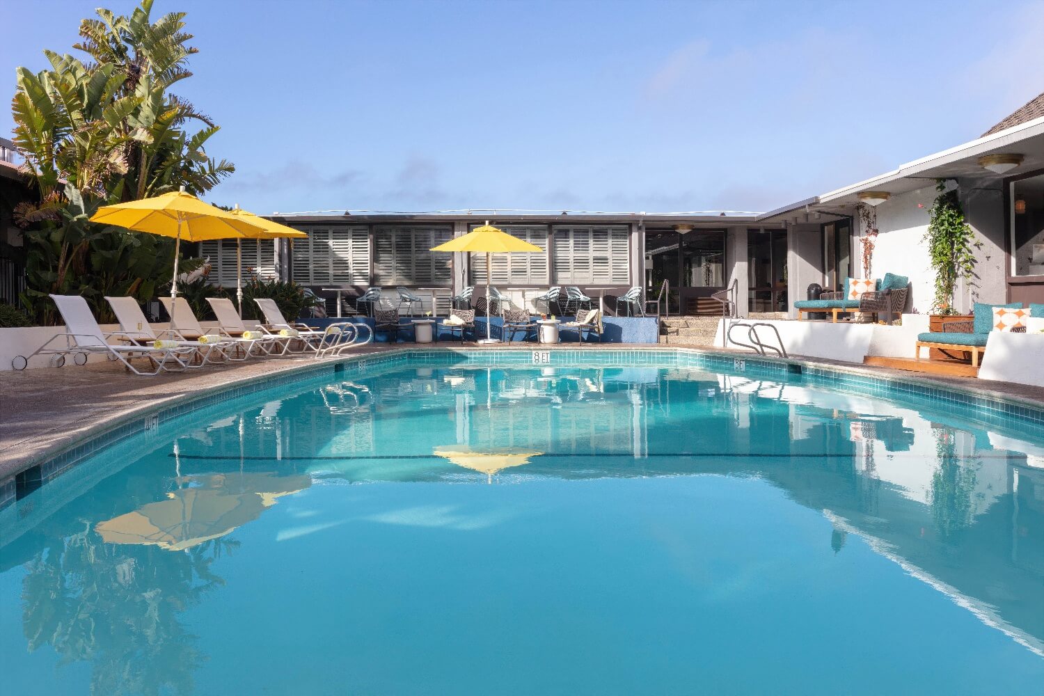 Heated outdoor pool in the central courtyard at Carmel Mission Inn, Carmel, California, with an 8-foot depth marker and yellow umbrellas along the deck.