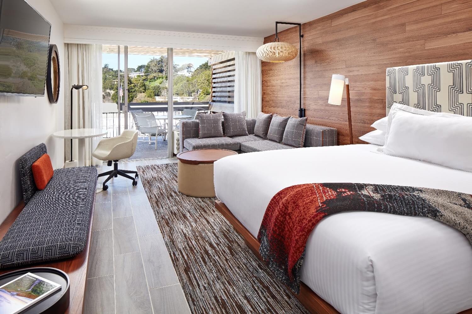 King Premiere room at Carmel Mission Inn, Carmel, California, with a wood-paneled accent wall, gray sectional, and sliding doors to a balcony.