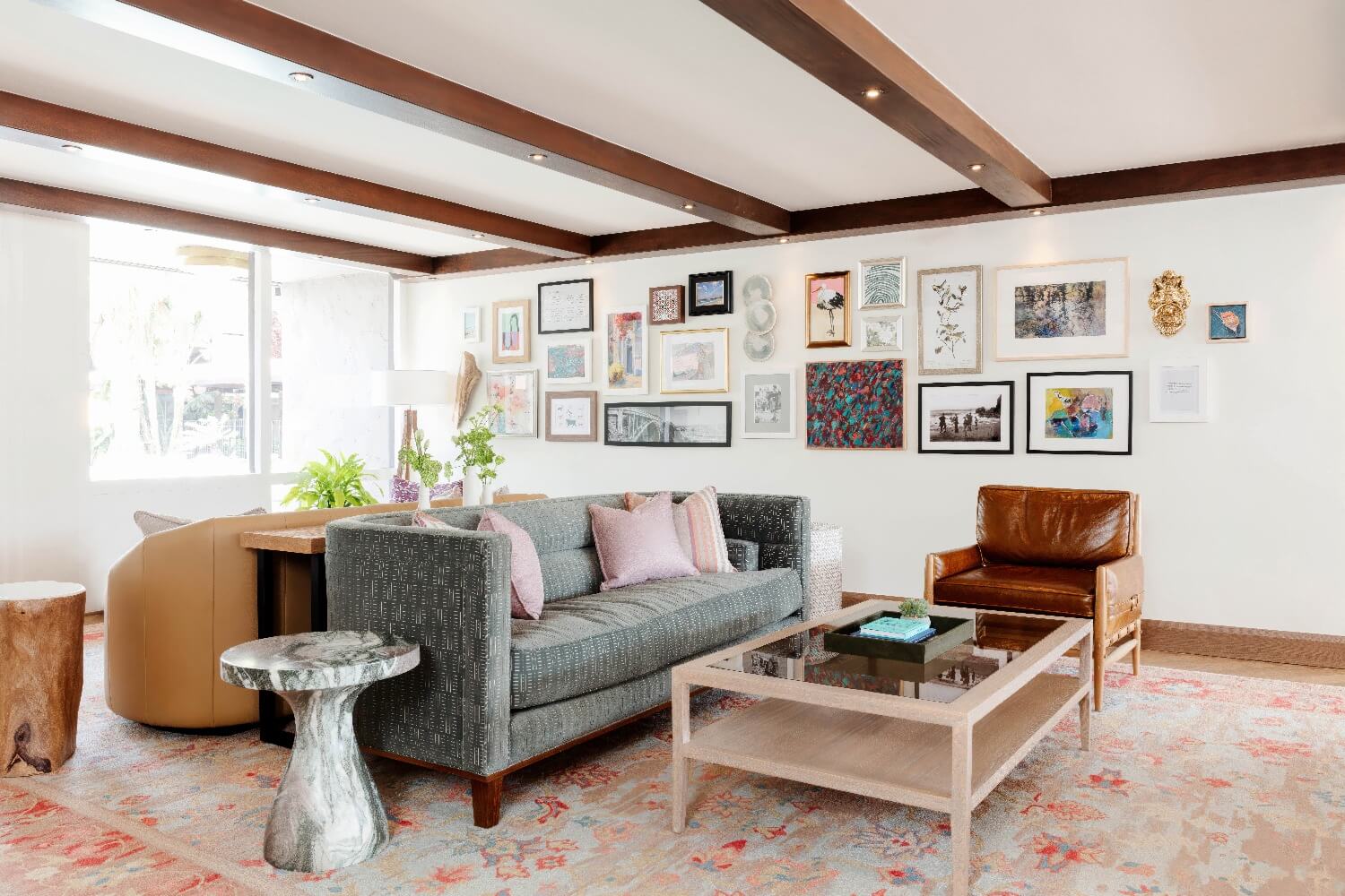 Lobby lounge with a gallery wall of framed art, exposed wood ceiling beams, and a gray sofa at Carmel Mission Inn, Carmel, California.