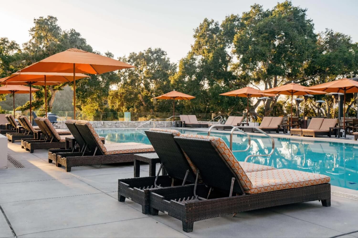Pool loungers and orange umbrellas beneath coast live oaks with glass railing at Carmel Valley Ranch, Carmel Valley