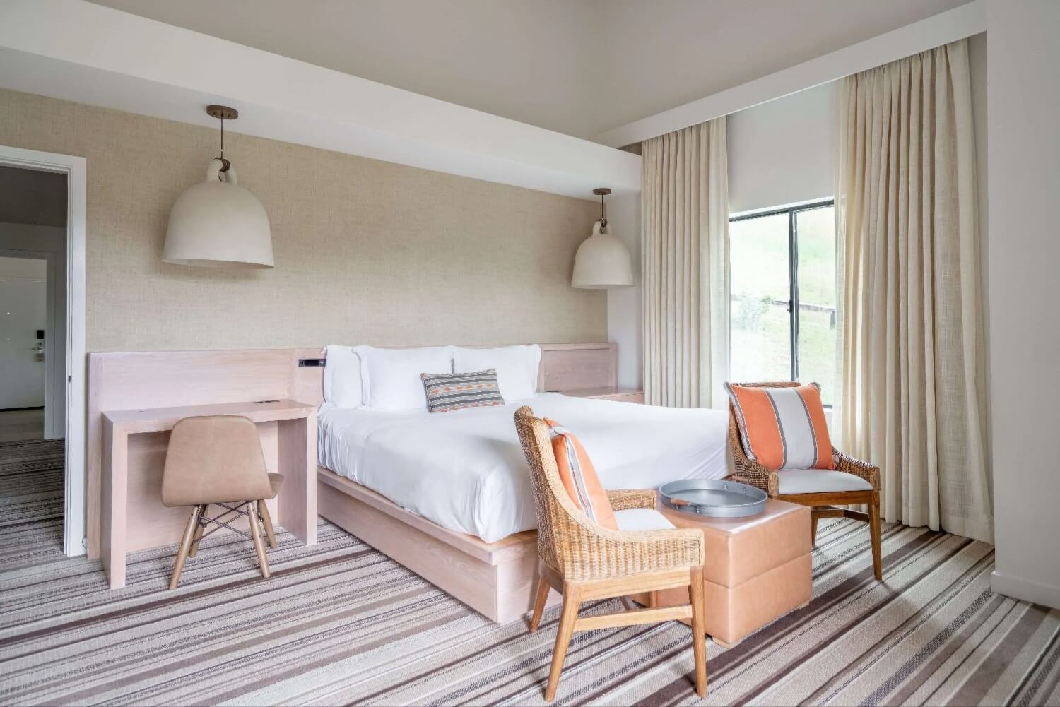 Suite bedroom with oak platform bed, bell pendant lights and wicker armchairs at Carmel Valley Ranch, Carmel Valley