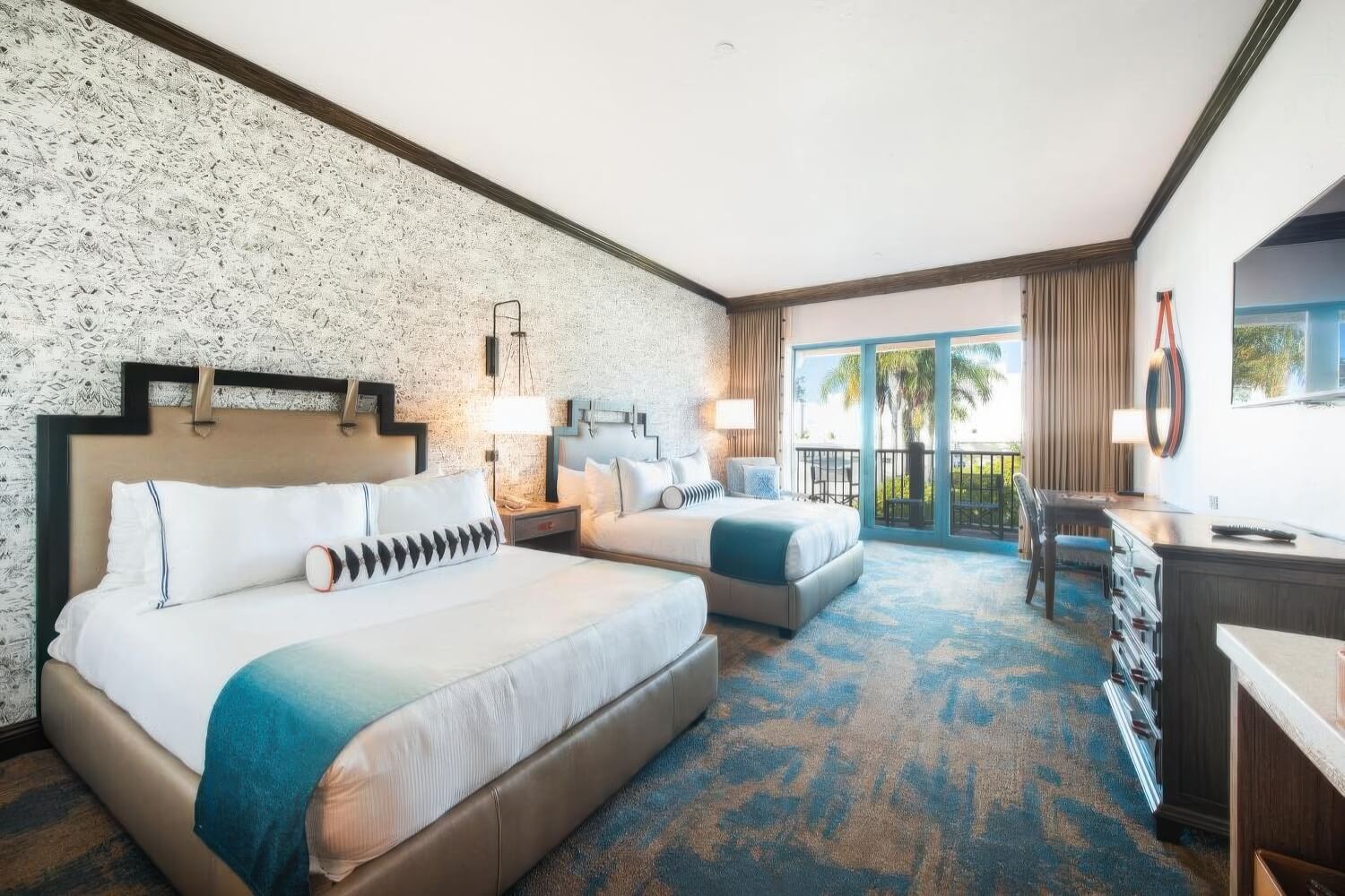 Guest room with two queen beds and a furnished balcony overlooking palms at Harbor View Inn, Santa Barbara.