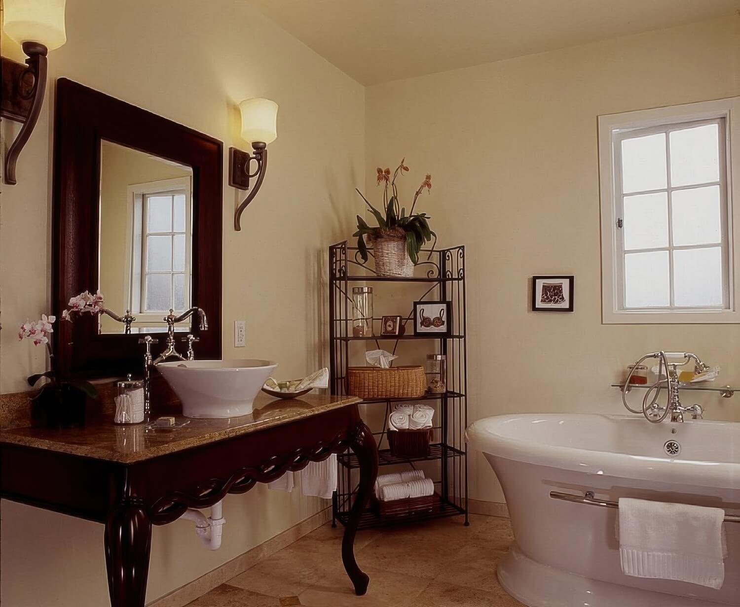 Freestanding white bathtub, a vessel sink on a carved dark-wood vanity, and a wrought-iron shelf of rolled towels in a guest bathroom at L'Auberge Carmel, Carmel-by-the-Sea.