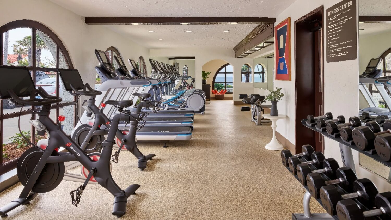 Fitness center with Peloton bikes, treadmills, and dumbbells in an arched-window room at Mar Monte Hotel, Santa Barbara.