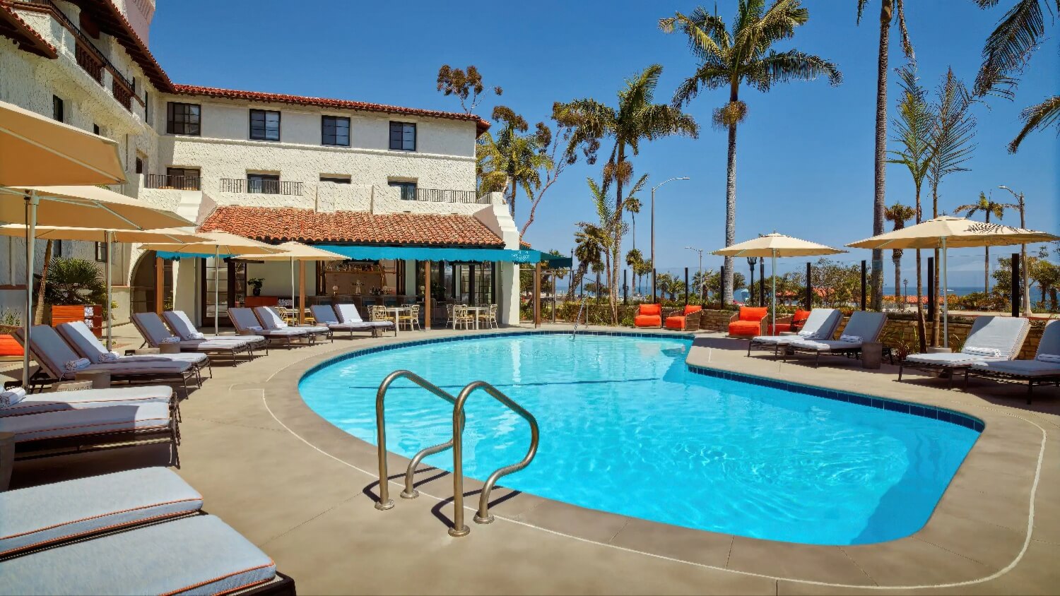 Heated outdoor pool ringed by umbrellas and loungers beneath the 1931 main building at Mar Monte Hotel, Santa Barbara.
