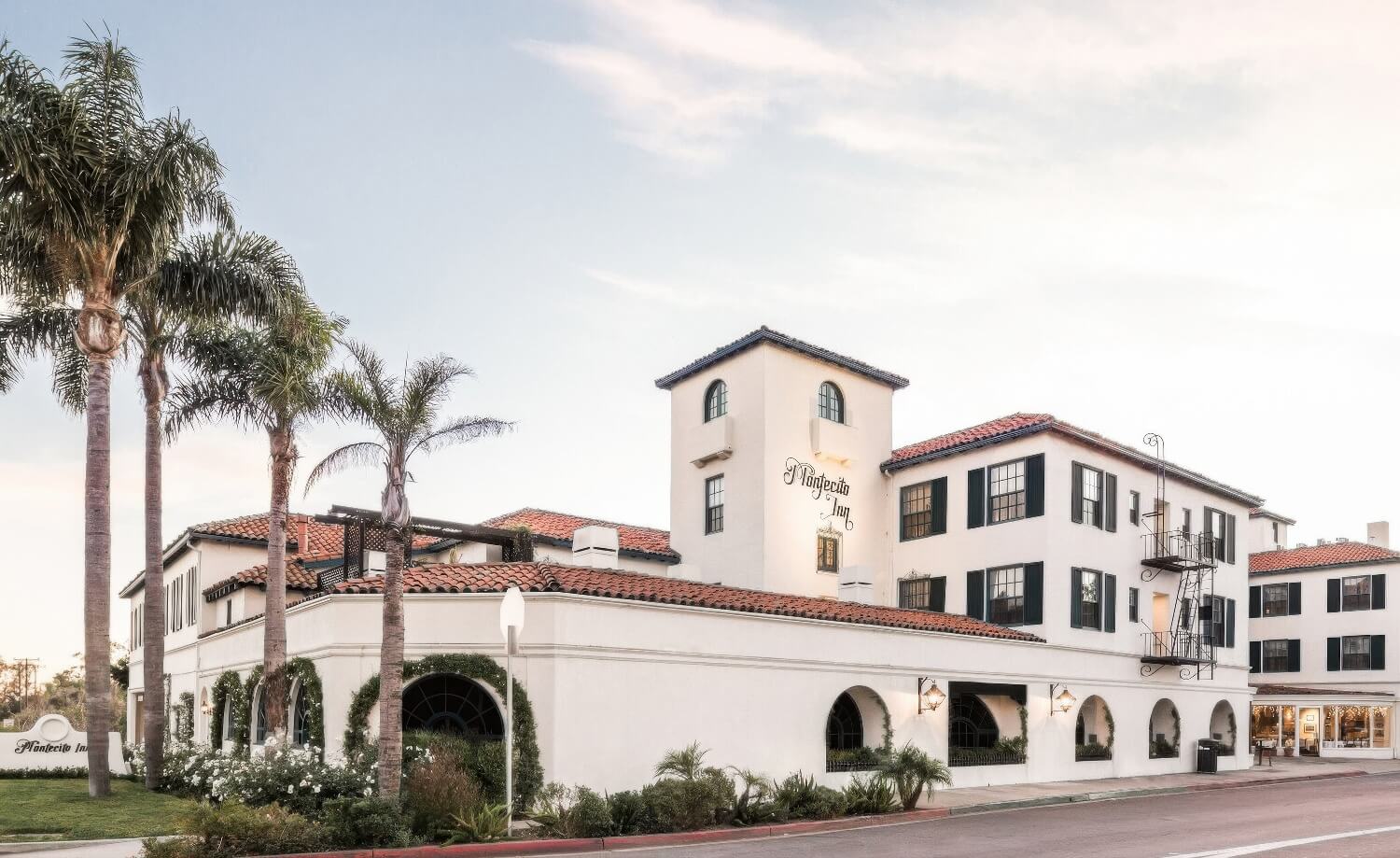 White Mediterranean Revival facade with red-tile roofs, signed tower and palms at the Montecito Inn, Montecito, at dusk