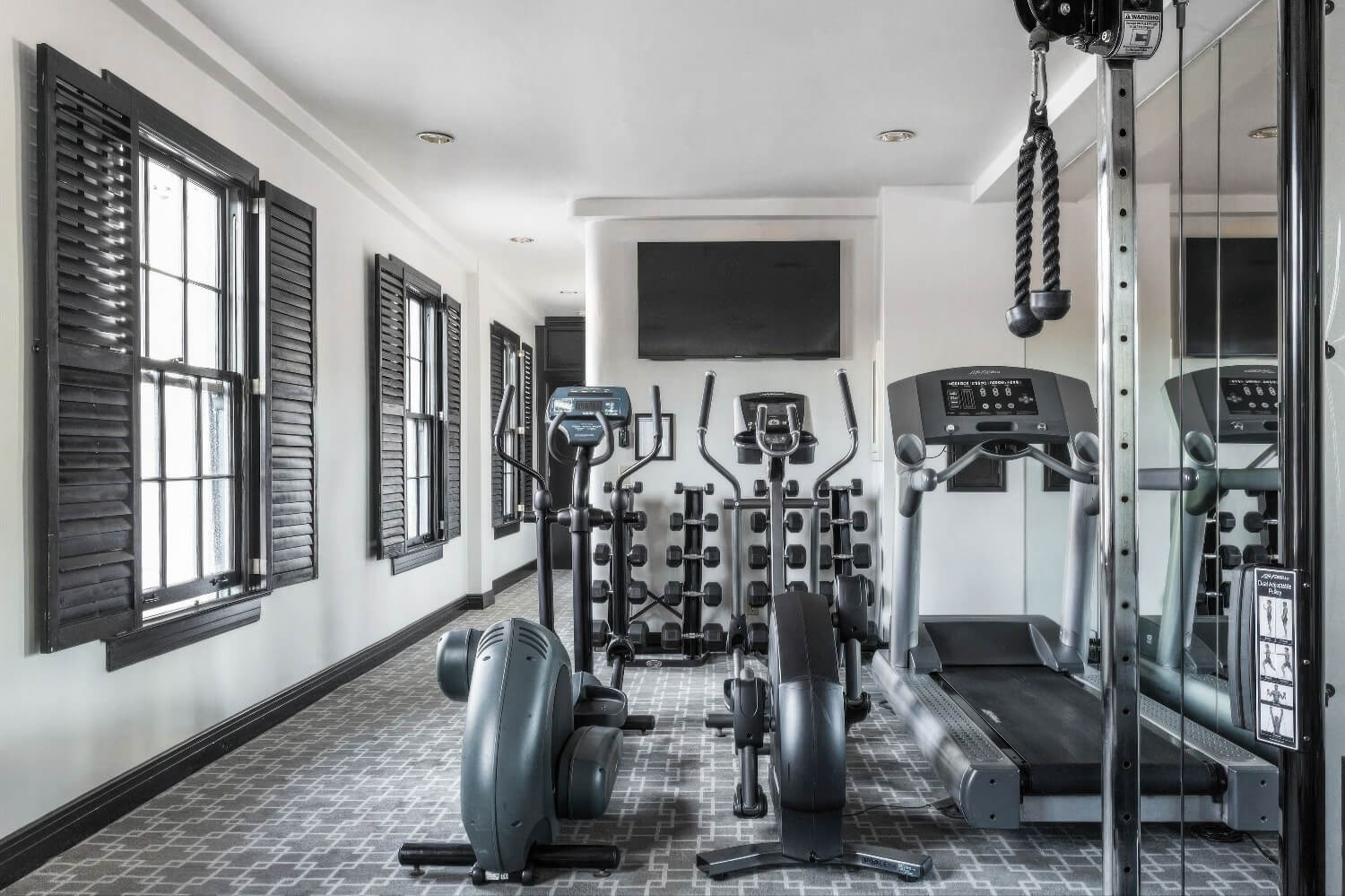 Compact fitness room with treadmill, two ellipticals, dumbbell rack and cable pulley at the Montecito Inn, Montecito