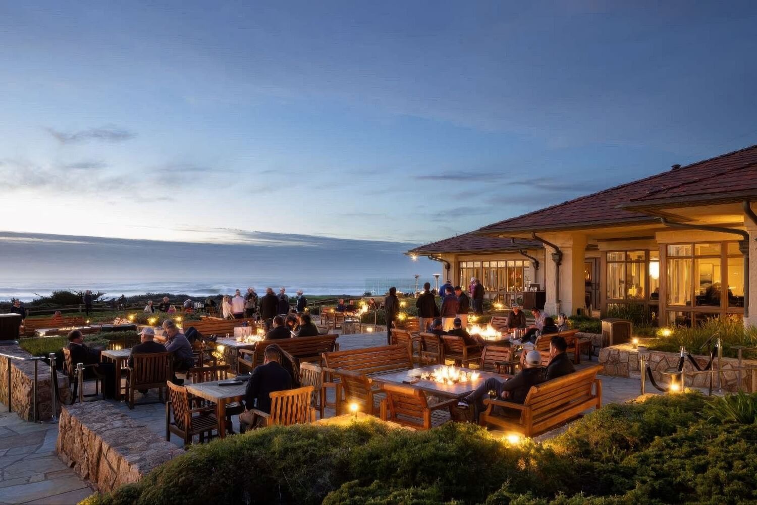 Guests around fire-pit tables on the ocean terrace at dusk at The Inn at Spanish Bay, Pebble Beach